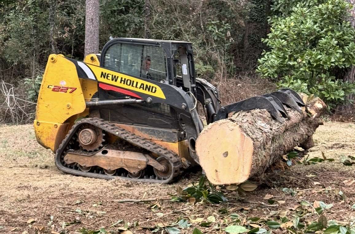 Skid steer carrying a big log section off a job